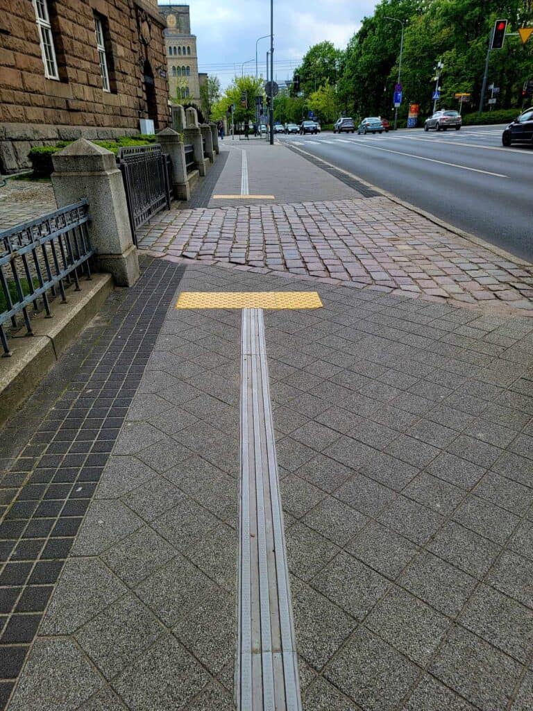 A street showing textured rubber tracking leading to a square pad with round bumps indicating an active driveway. The bumps and track continue on the other side.