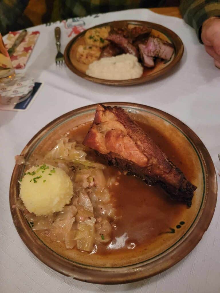 A brown plate with a potato dumpling, cabbage, and a crispy pork shoulder