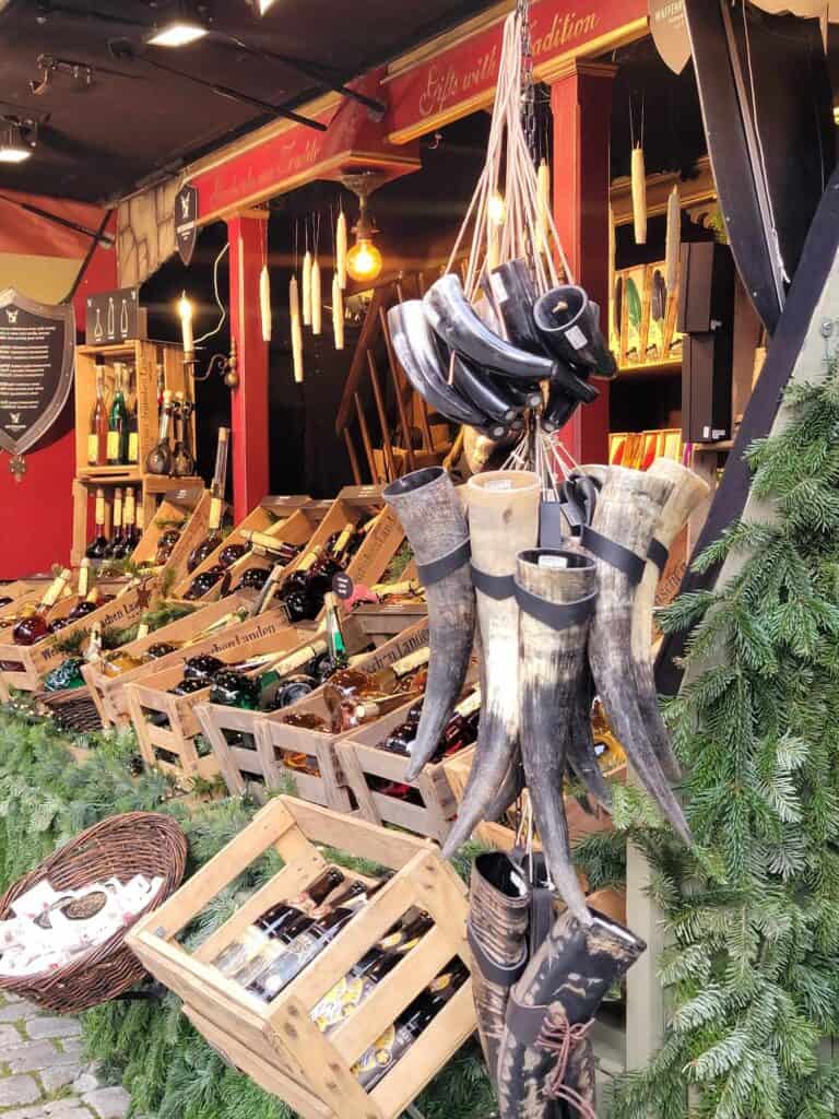 A christmas market stall with wooden crates filled with bottles of colored liquids, and drinking vessels made of cow horns