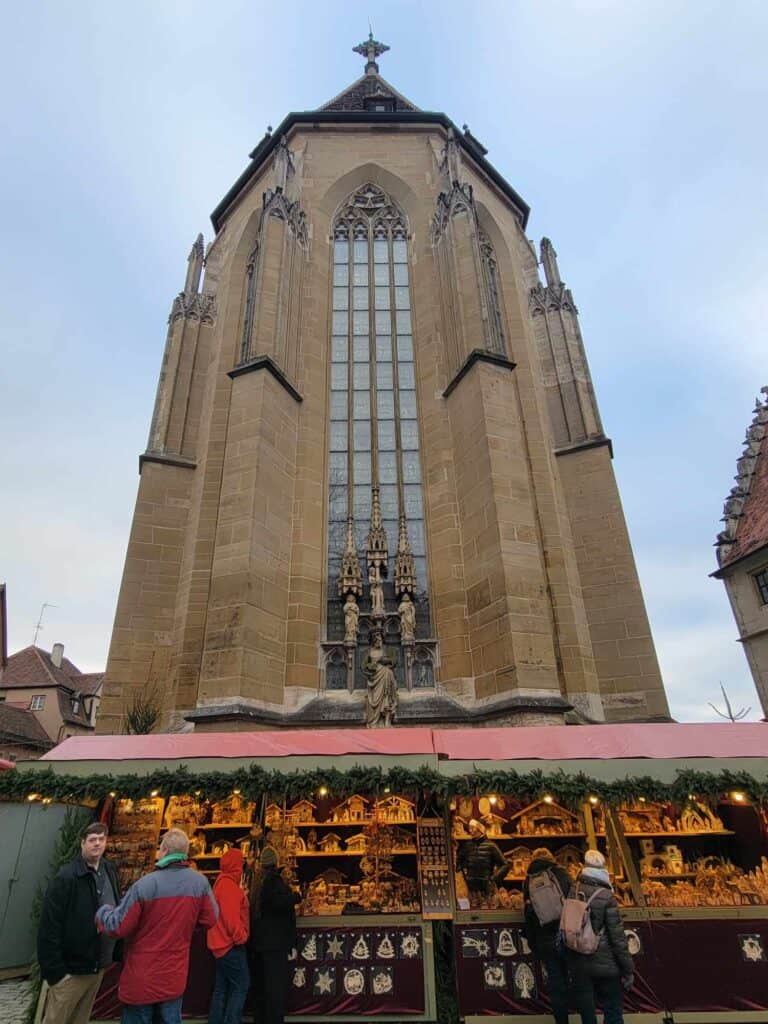 A christmas market stall featuring carved wooden decorations and nativity scenes in front of a tall medieval church