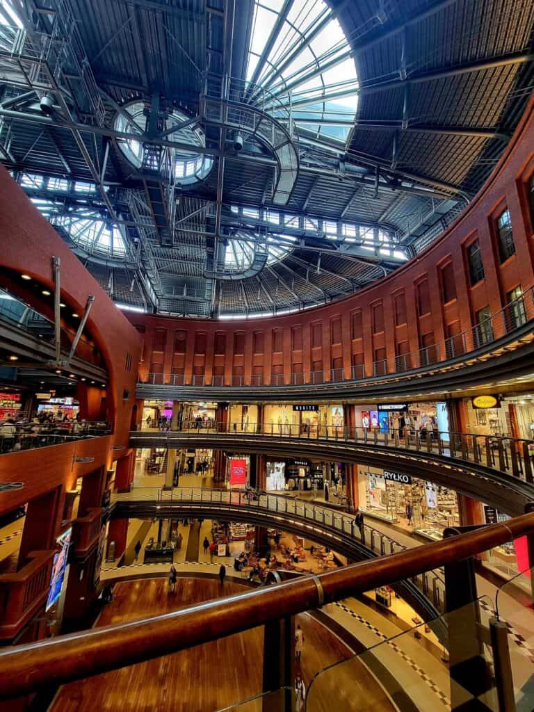 The interior of a shopping mall with sweeping curves and multi levels with an open center and an elaborate metal grillework ceiling