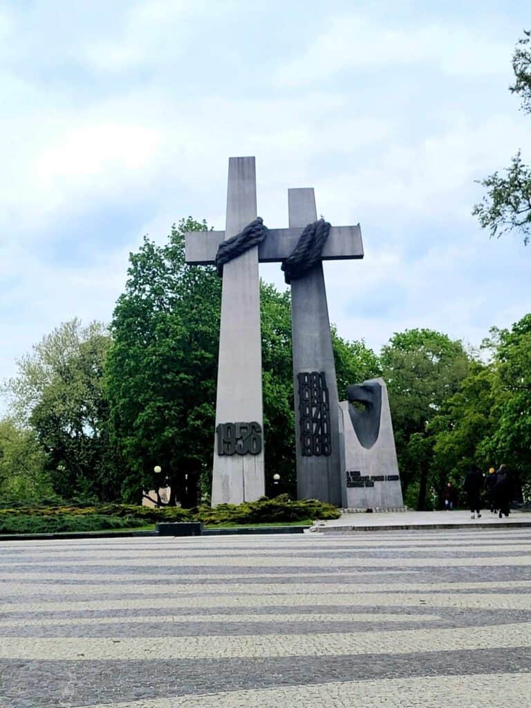 Two huge grey cross sculptures with rope slung around the intersection of the crosses. One says 1956