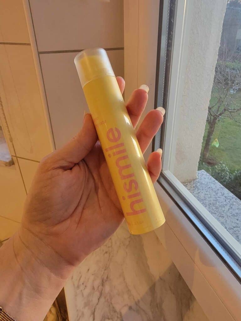 A woman's hand holds an upright plastic round yellow tube of banana toothpaste