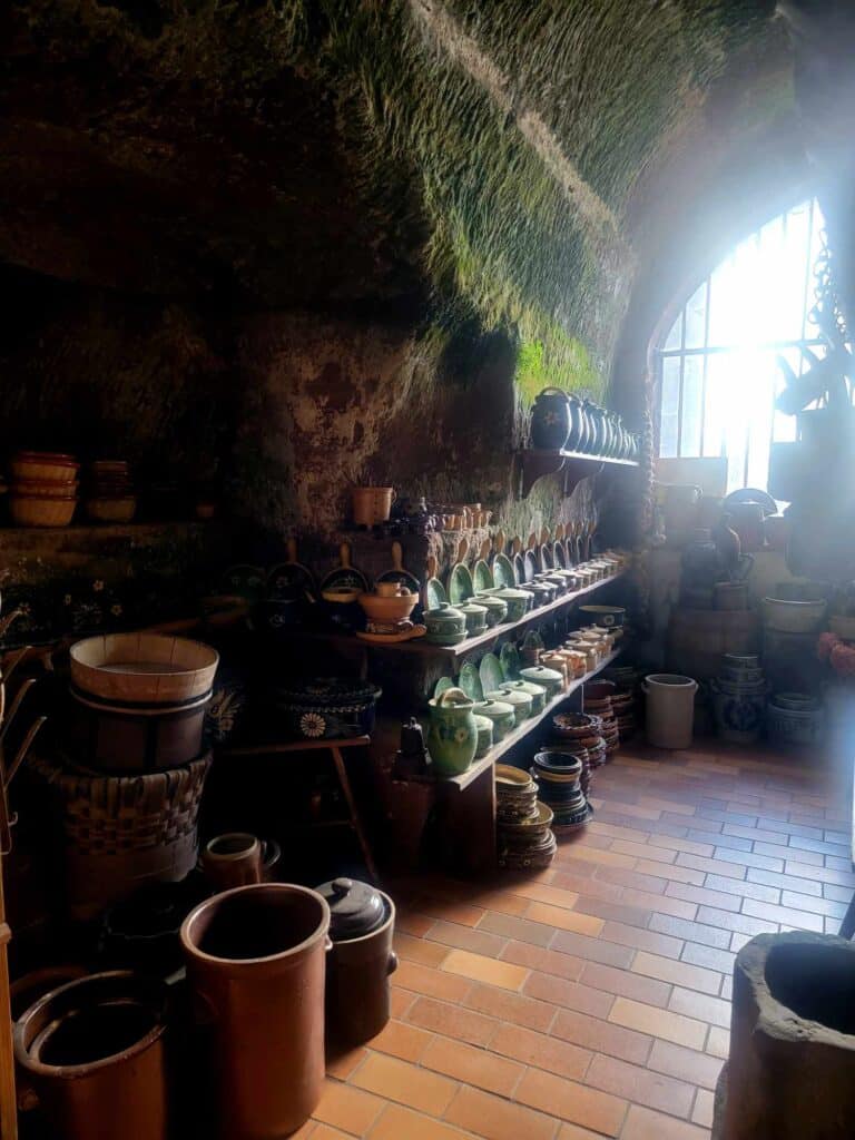 A medieval kitchen with shelves stacked with earthenware pots and kitchen items