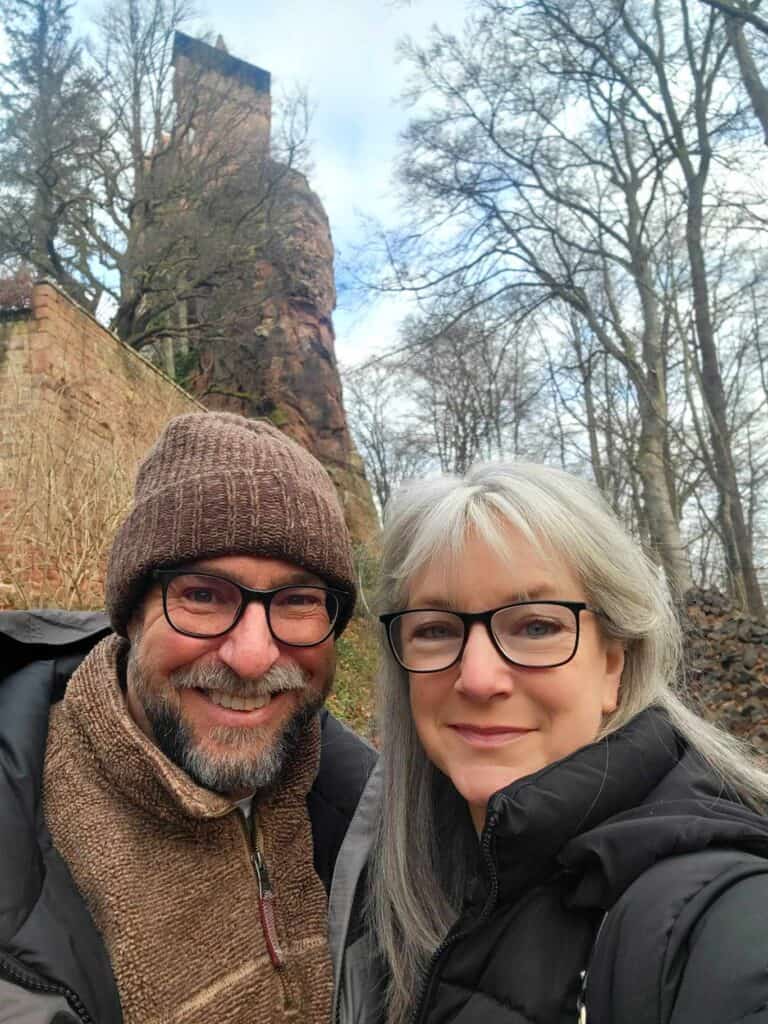 A smiling couple in winter coats takes a selfie with the castle tower behind them.