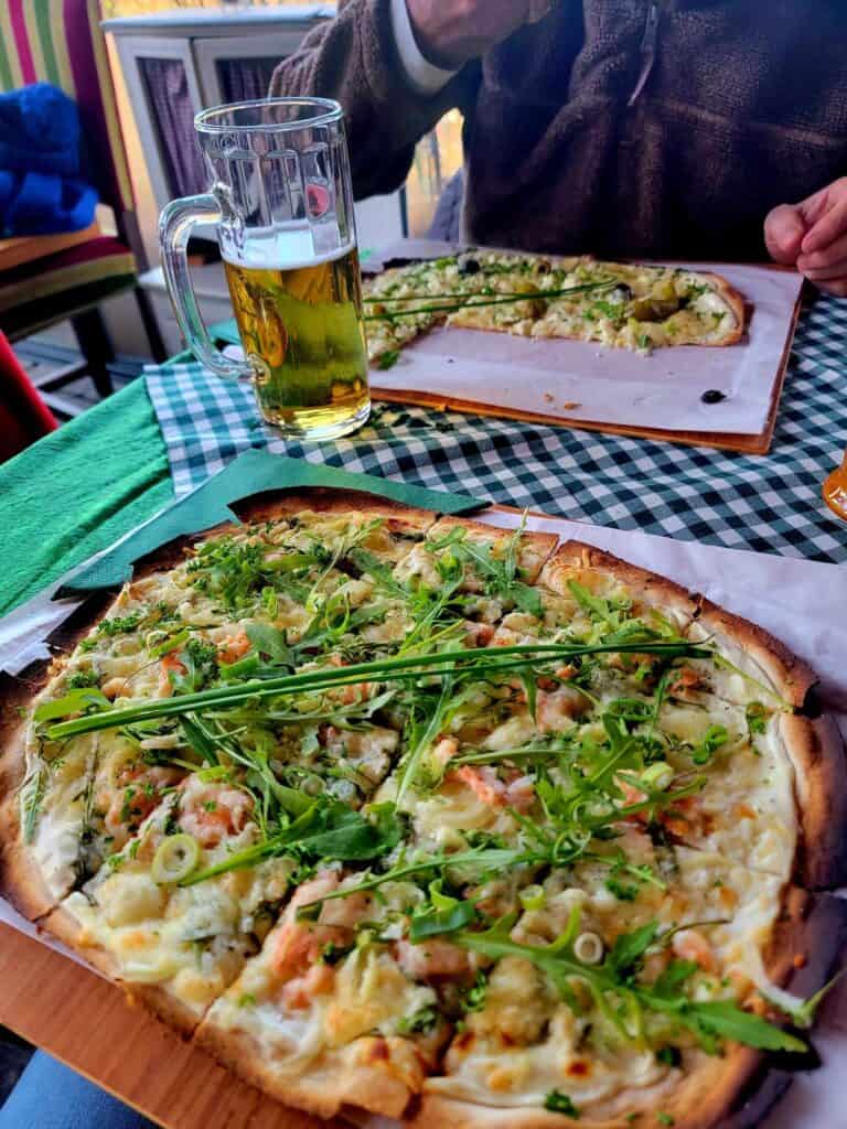 A flammkuchen with smoked salmon, arugula, green onions. Another across the table and a half drunk mug of light beer