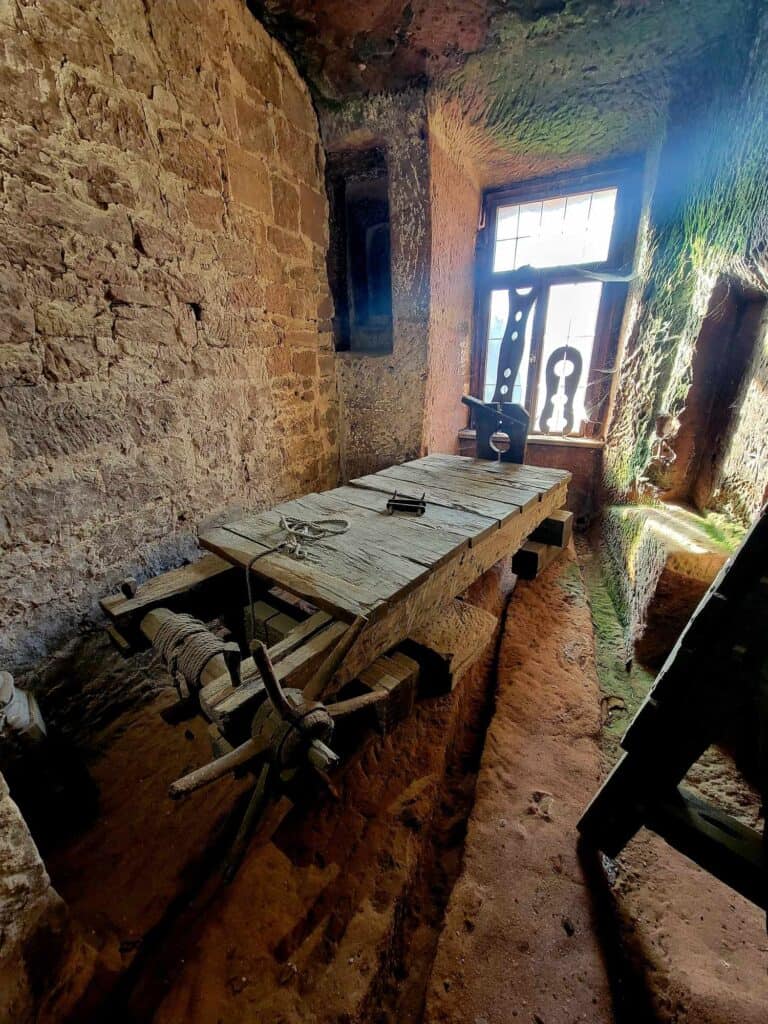 A wooden rack with planks across the top and a wooden winding mechanism, Contraptions in the window for holding arms and legs.