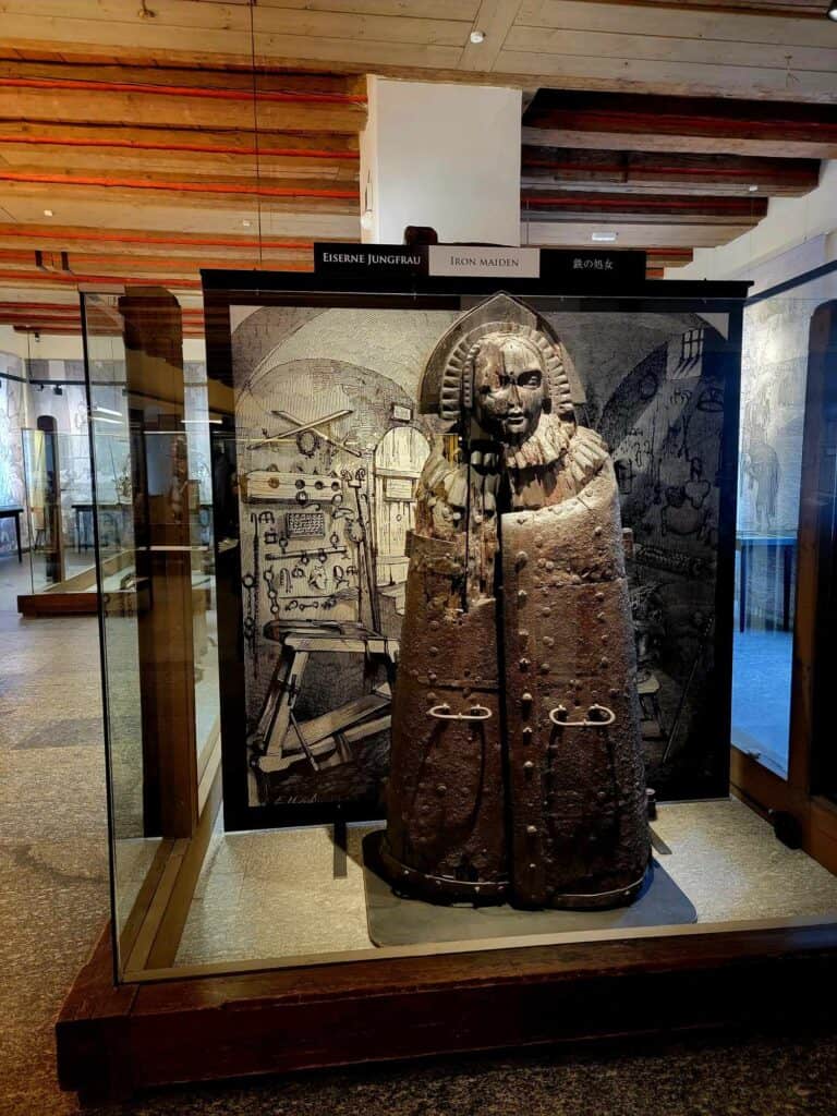 An "iron maiden" which looks like a large cabinet in the shape of a human form with a woman's head and a cloak