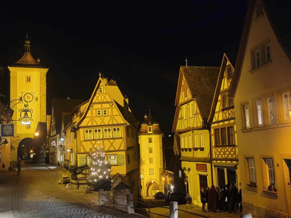 A nighttime shot of the Plonlein with the medieval clock tower, and half timbered houses on a forked cobblestone street.