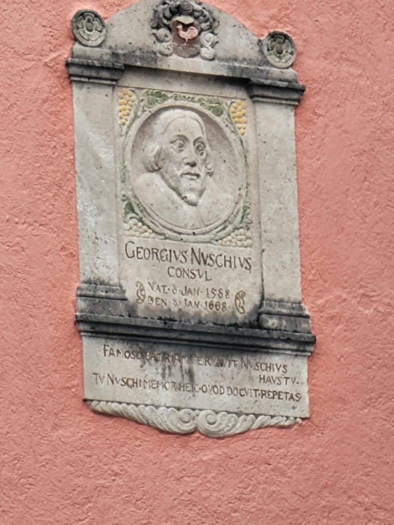 A man's face in relief on a stone plaque affixed to a pink building