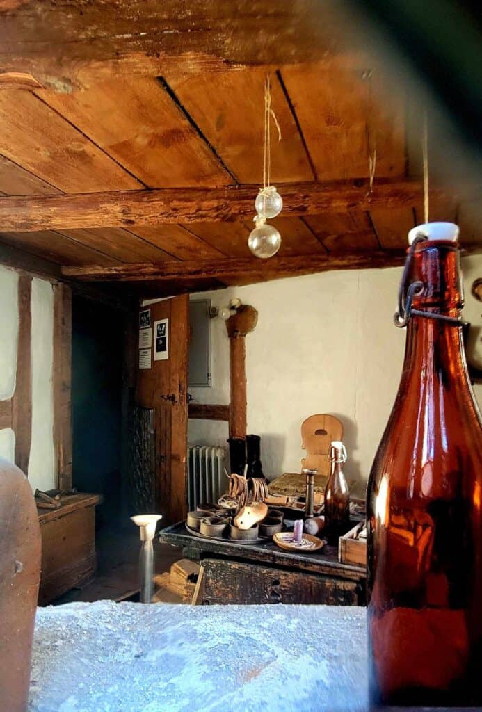 A table with a candle, and shoemaking equipment, a wood beam ceiling