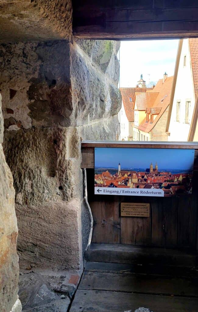 A stone door on the left with a sign showing a panoramic view of the city from above and the words Eingang/Entrance Röderturm