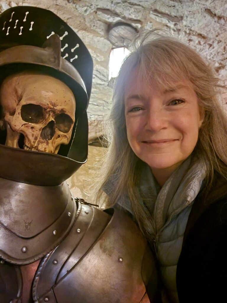 A woman smiles next to a skeleton in a suit of armor