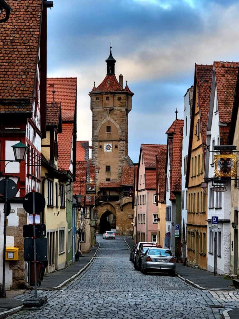 A cobblestone street with timbered houses and a medieval tower made of sandstone