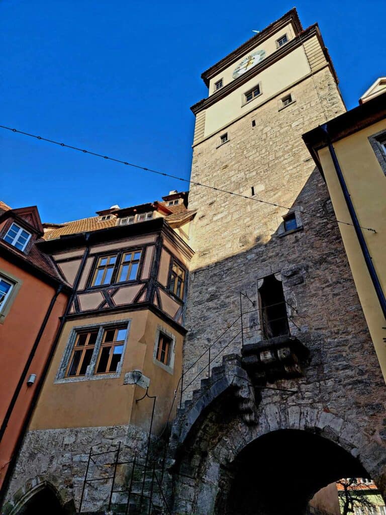 Looking up at a pale stone tower attached to a timbered house with an arched gate