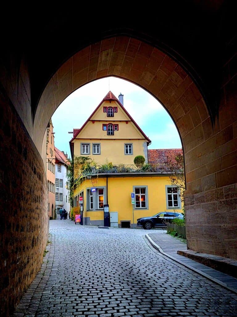 A stone archway with a yellow medieval house framed in the center