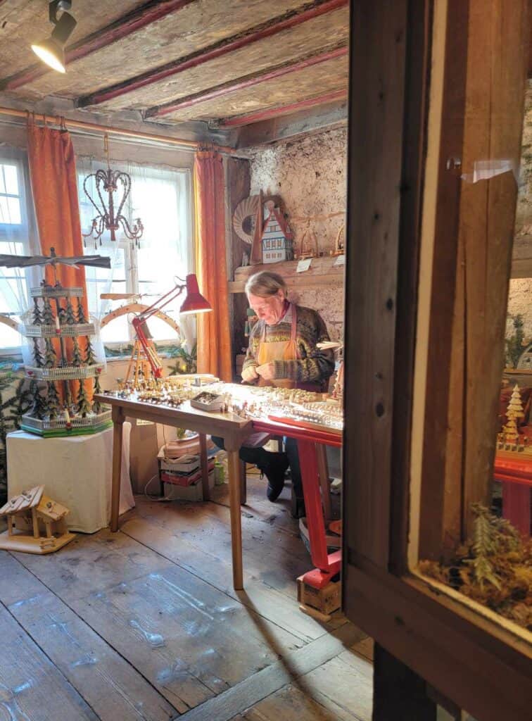 A woodworker in coveralls in a very old woodworking shop looks at an object he is making