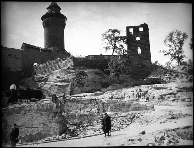 A black and white image of the castle in 1945 showing bomb damage to the right hand tower, and a person standing in the road looking up