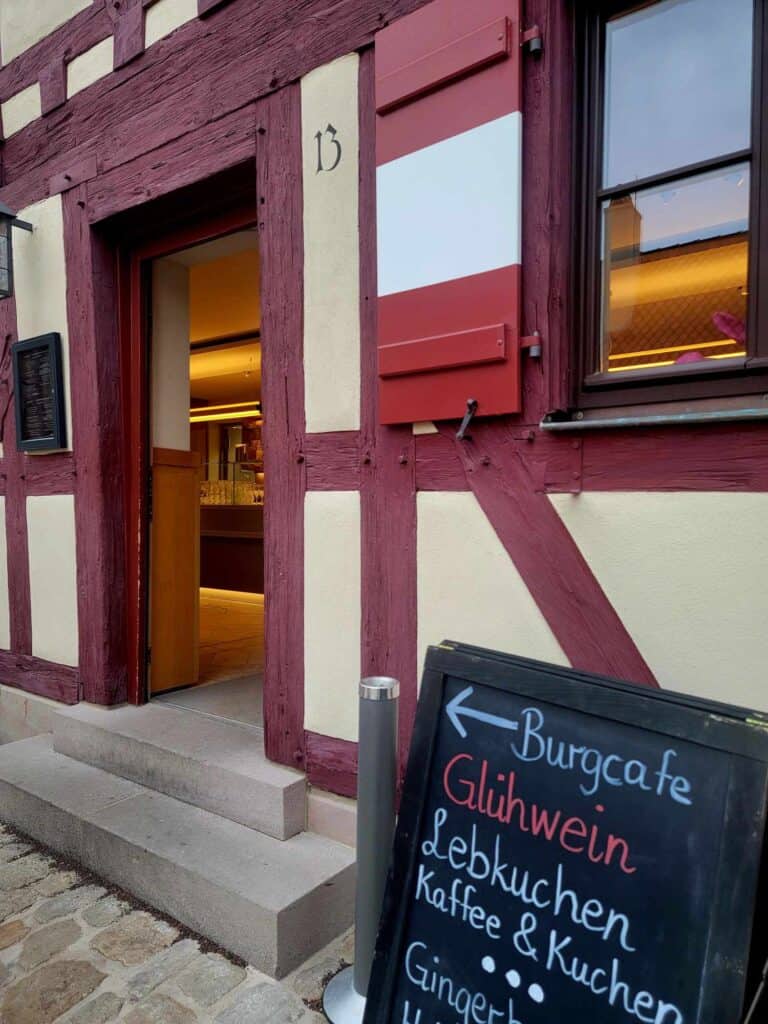 A sign pointing to an open door of a timbered building reads: Burgcafe Glühwein, Lebkuchen, Kaffee & Kuchen