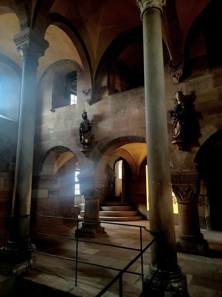 A moody two story room with sculptures on the walls, and columns of white marbe with floors and walls of red and yellow sandstone