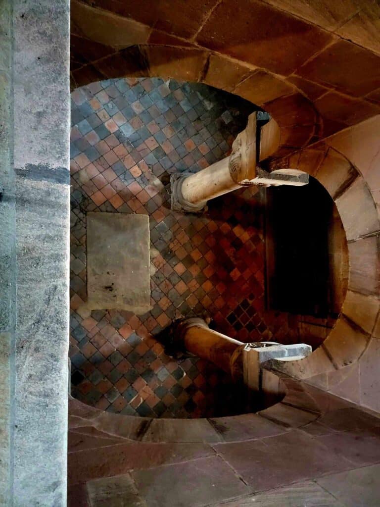 Looking over the edge of a balcony to the original red and black stone floors of the castle and an archway supported by columns