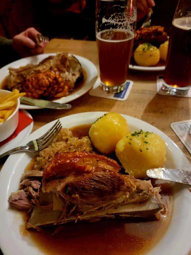 Pork shoulder (Schauefele) with two potato dumplings sits on a table with beer and fries