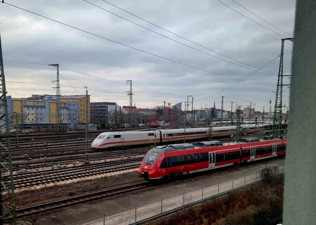 Many train tracks and wires and two trains in motion, one red and one white