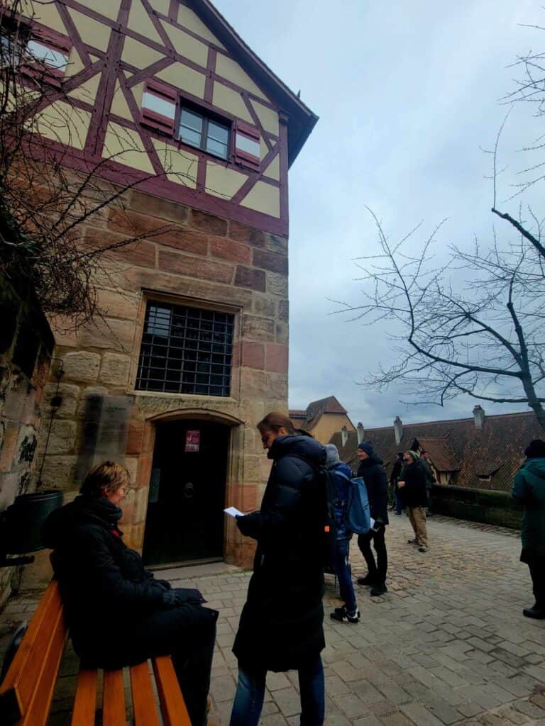 A sandstone building with half timbering and people waiting 