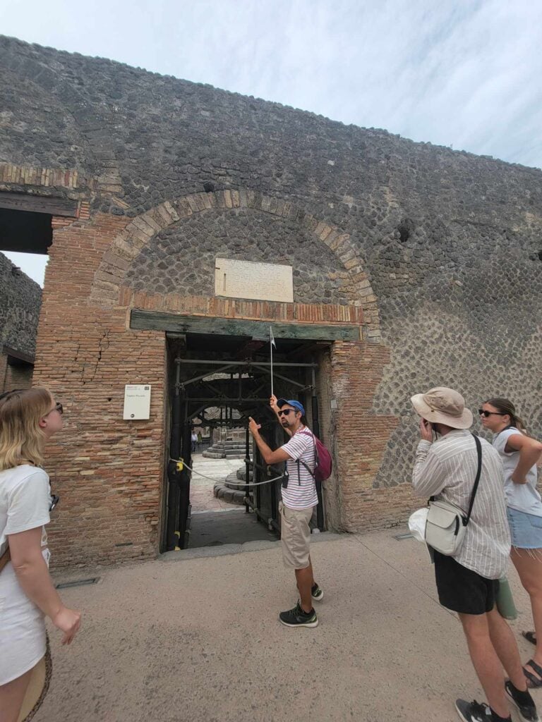 Pompeii vs. Herculaneum: Best Tips & Biggest Differences 32 A guide stands at a portal in Pompeii pointing to a sign while his tour group looks on