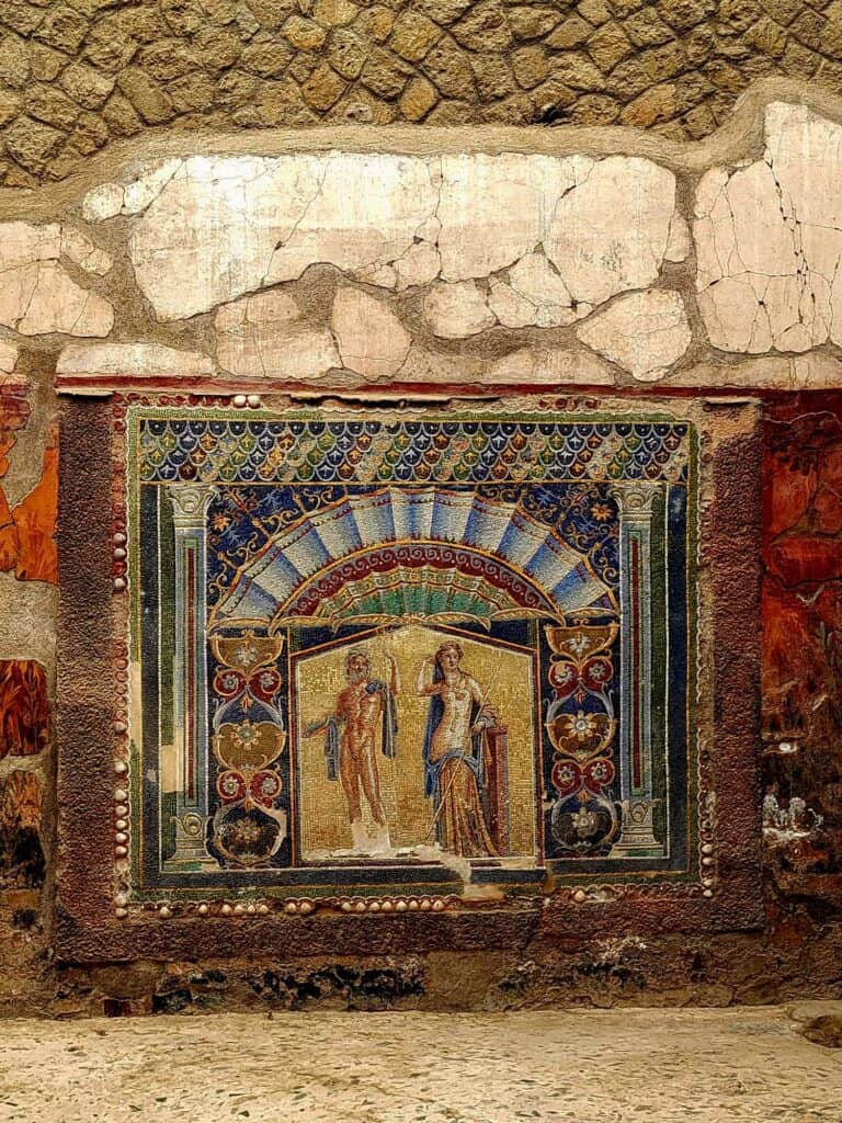 Pompeii vs. Herculaneum: Best Tips & Biggest Differences 6 A sumptuous mosaic of two figures on a wall in deep and pale blue, gold, and red.