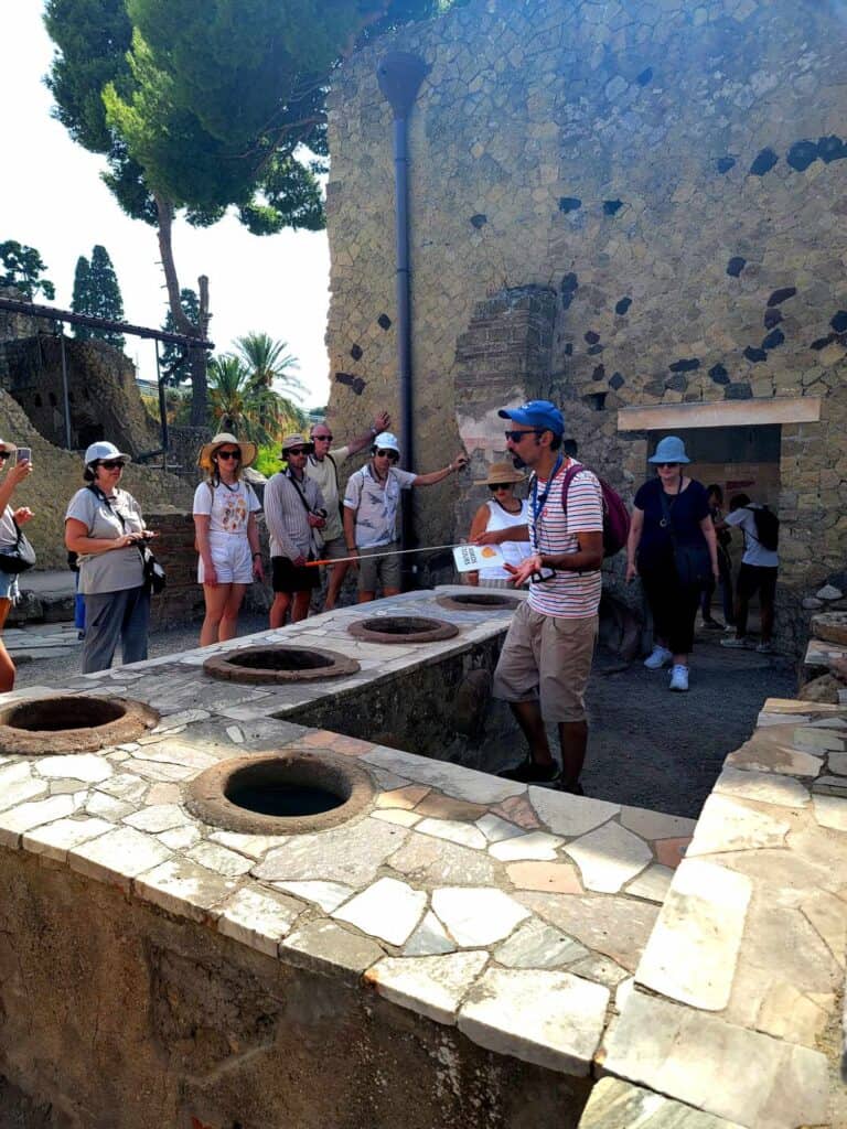Pompeii vs. Herculaneum: Best Tips & Biggest Differences 31 A guide stands behind the stone counter of a restaurant in Herculaneum talking to his tour group