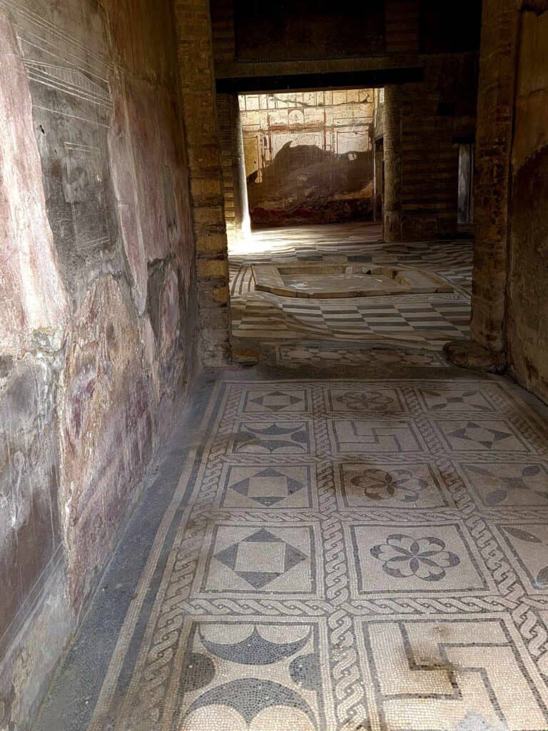 Pompeii vs. Herculaneum: Best Tips & Biggest Differences 19 An intricate stone mosaic floor in a building with three rooms visible