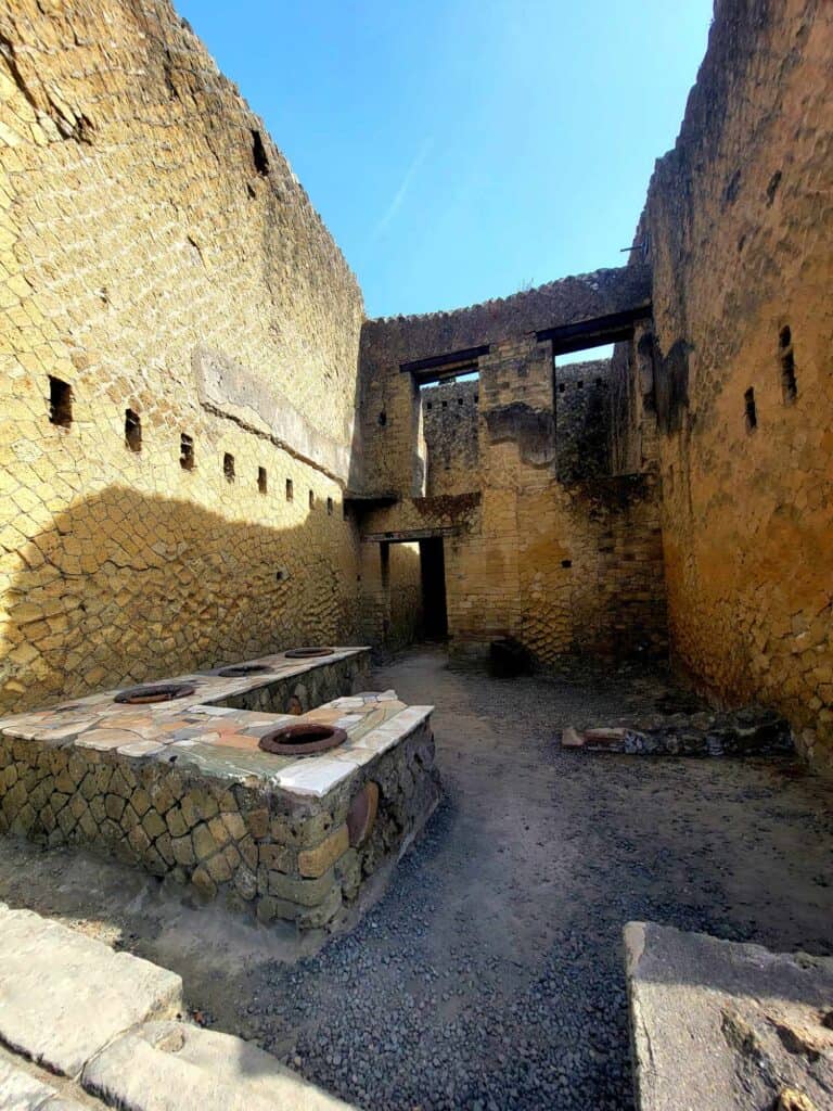Pompeii vs. Herculaneum: Best Tips & Biggest Differences 13 A shaded room in Herculaneum which used to be a restaurant with counter and food containers