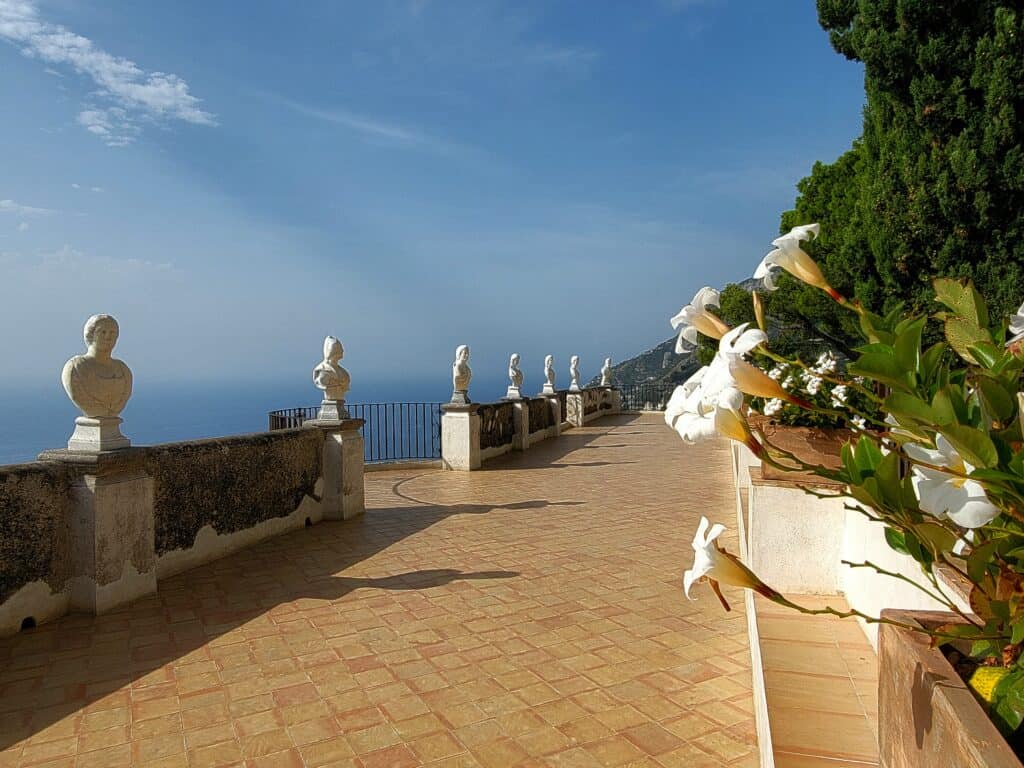 Villa Cimbrone Gardens: The Most Breathtaking View in Italy! 2 The Terrace of Infinity in Villa Cimbrone Gardens overlooking the ocean with travertine tiles, a row of white marble sculptures, and white lilies in bloom