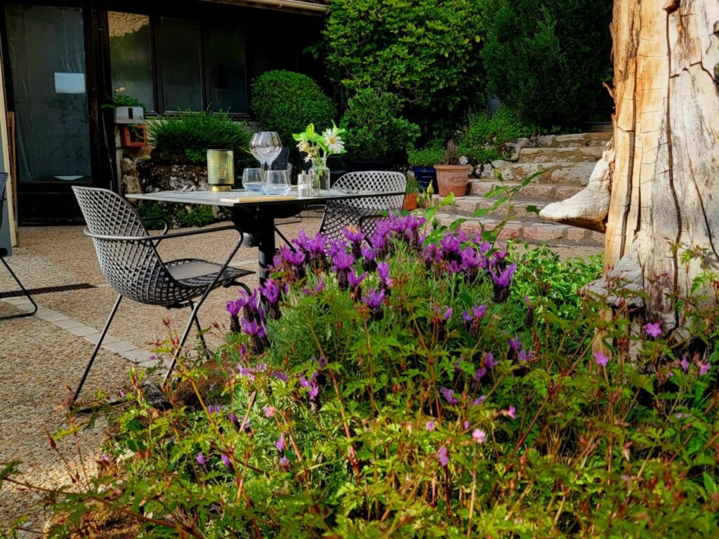 Best 2 Day Dordogne Prehistory Itinerary: What to See & Do 9 A table and chairs in a courtyard garden surrounded by greenery, stone stairs, and a patch of blooming lavender