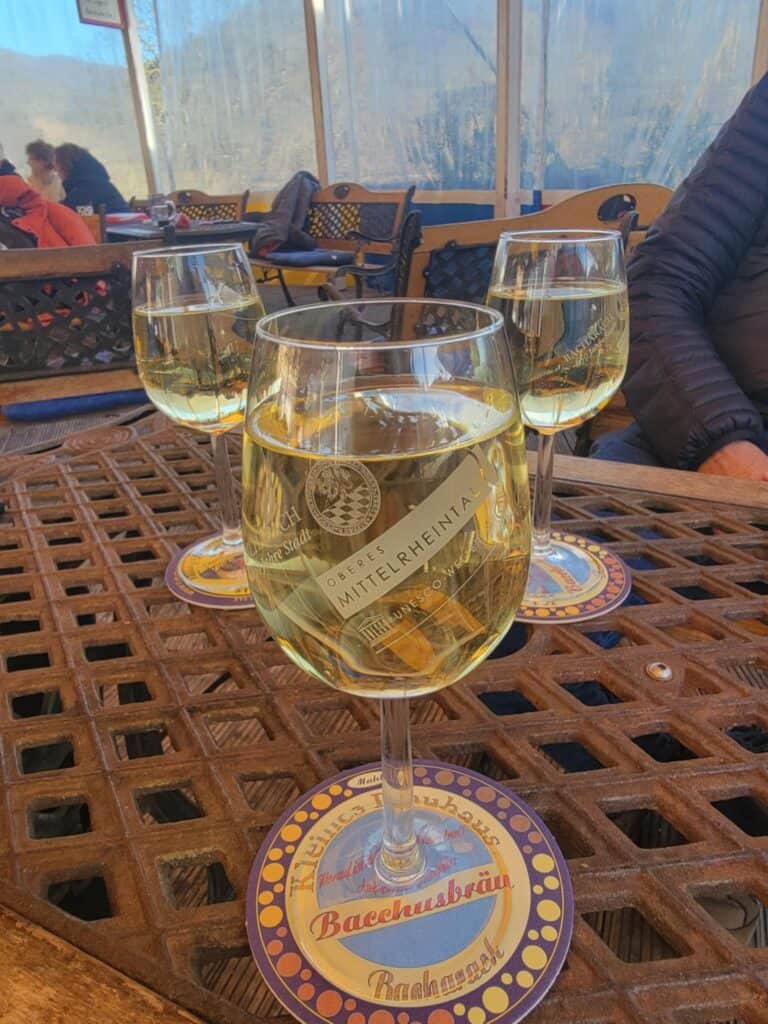 One Day in Bacharach: Best Guide to Germany's Hidden Gem on the Rhine 3 3 glasses of white wine on a wooden latticed table with coasters that say Bachhusbräu