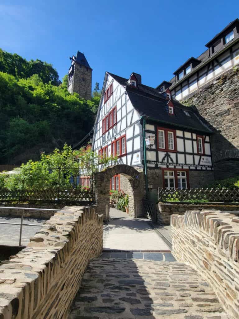 One Day in Bacharach: Best Guide to Germany's Hidden Gem on the Rhine 18 A green and red half timbered house with a stone archway leading to a rose garden see from the vantage point of a wooden stone bridge