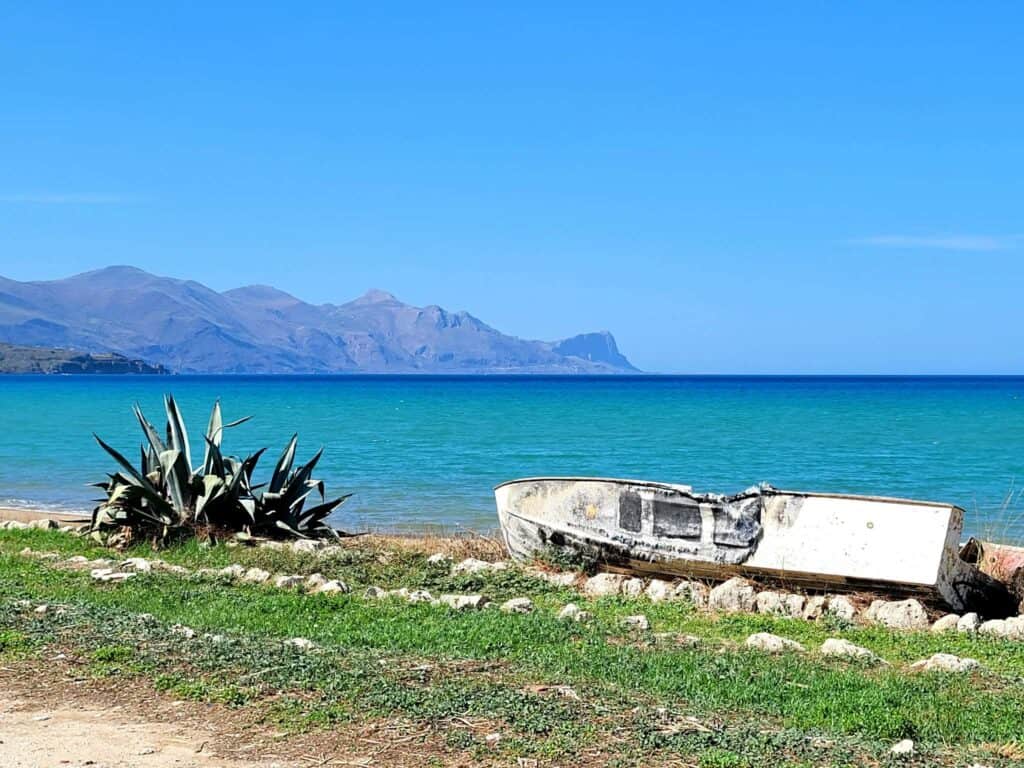 An old boat on a Sicilian beach with blue water and mountains