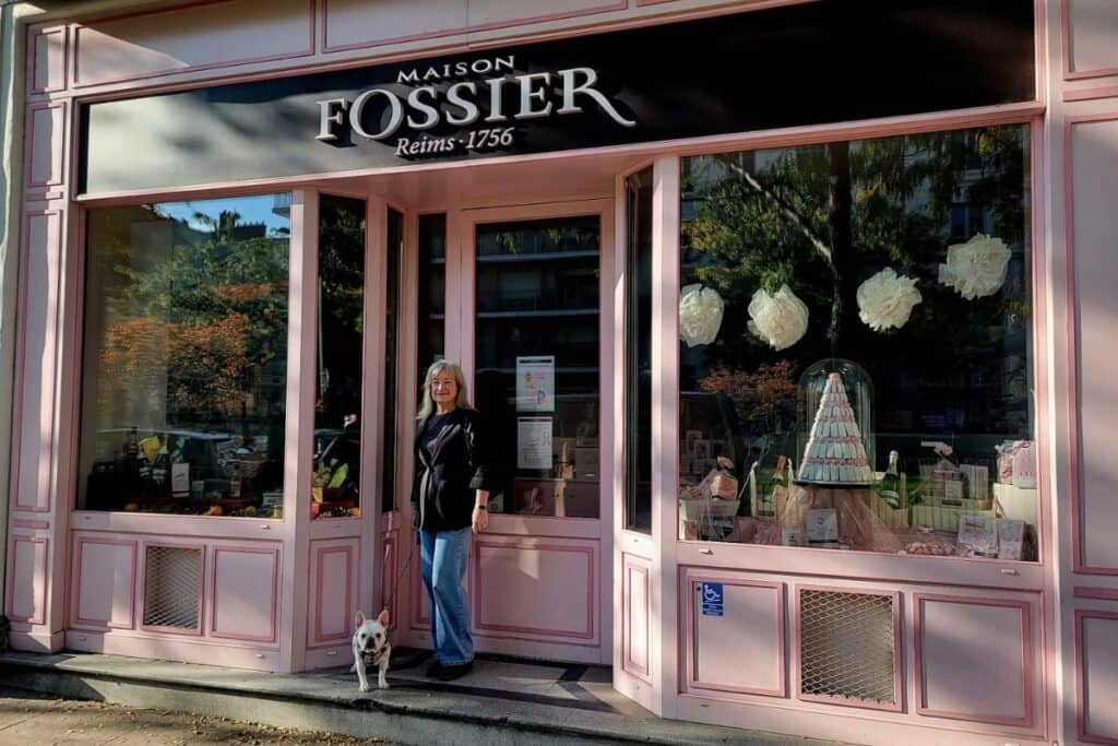 A woman and a white frenchie stand in the doorway of Maison Fossier in Reims France