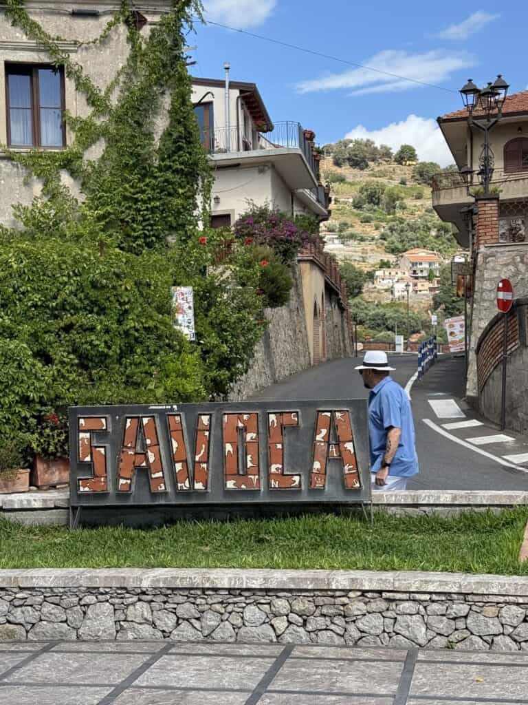 Man walking by a Savoca sign in Savoca Sicily